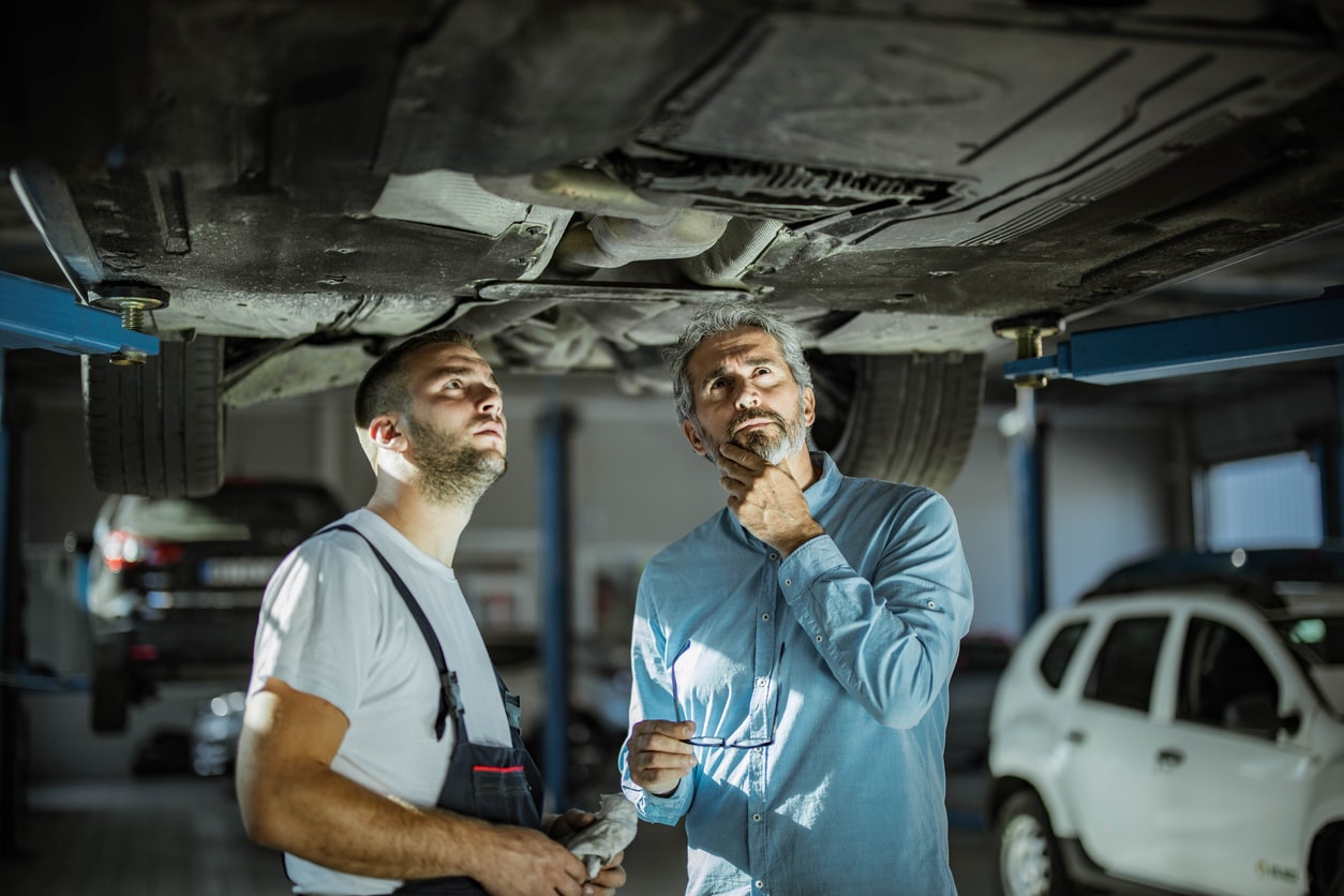 Mid adult customer and auto repairman analyzing chassis in a workshop.