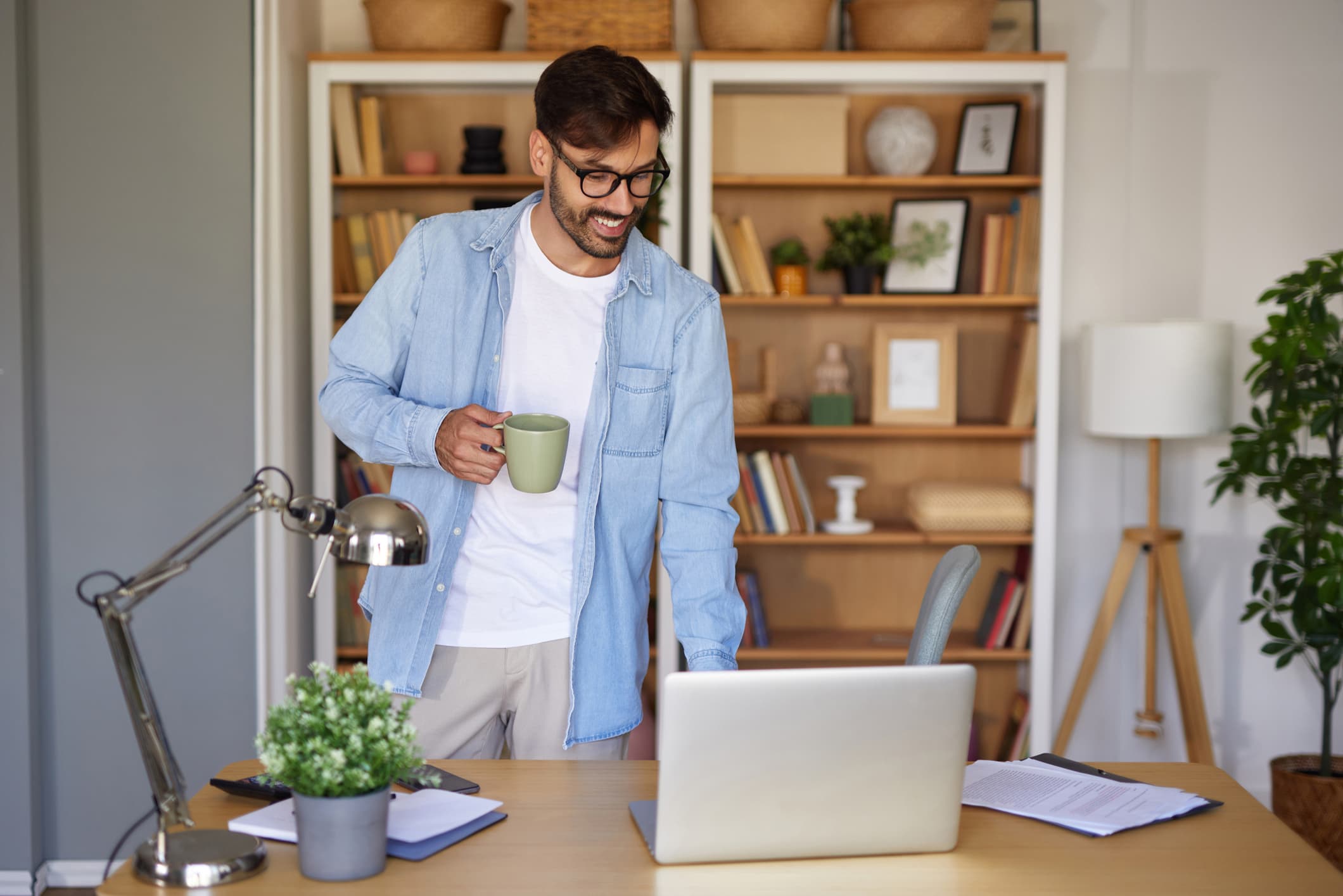 Νέος άνδρας πίνει καφέ από την κούπα του ενώ βρίσκεται στο γραφείο του στο σπίτι